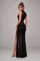 Woman wearing a black lace and sequin evening gown against a gray background