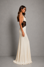 A woman modeling a floor-length ivory gown with a black lace waist panel, shown in side profile against a plain gray studio background.