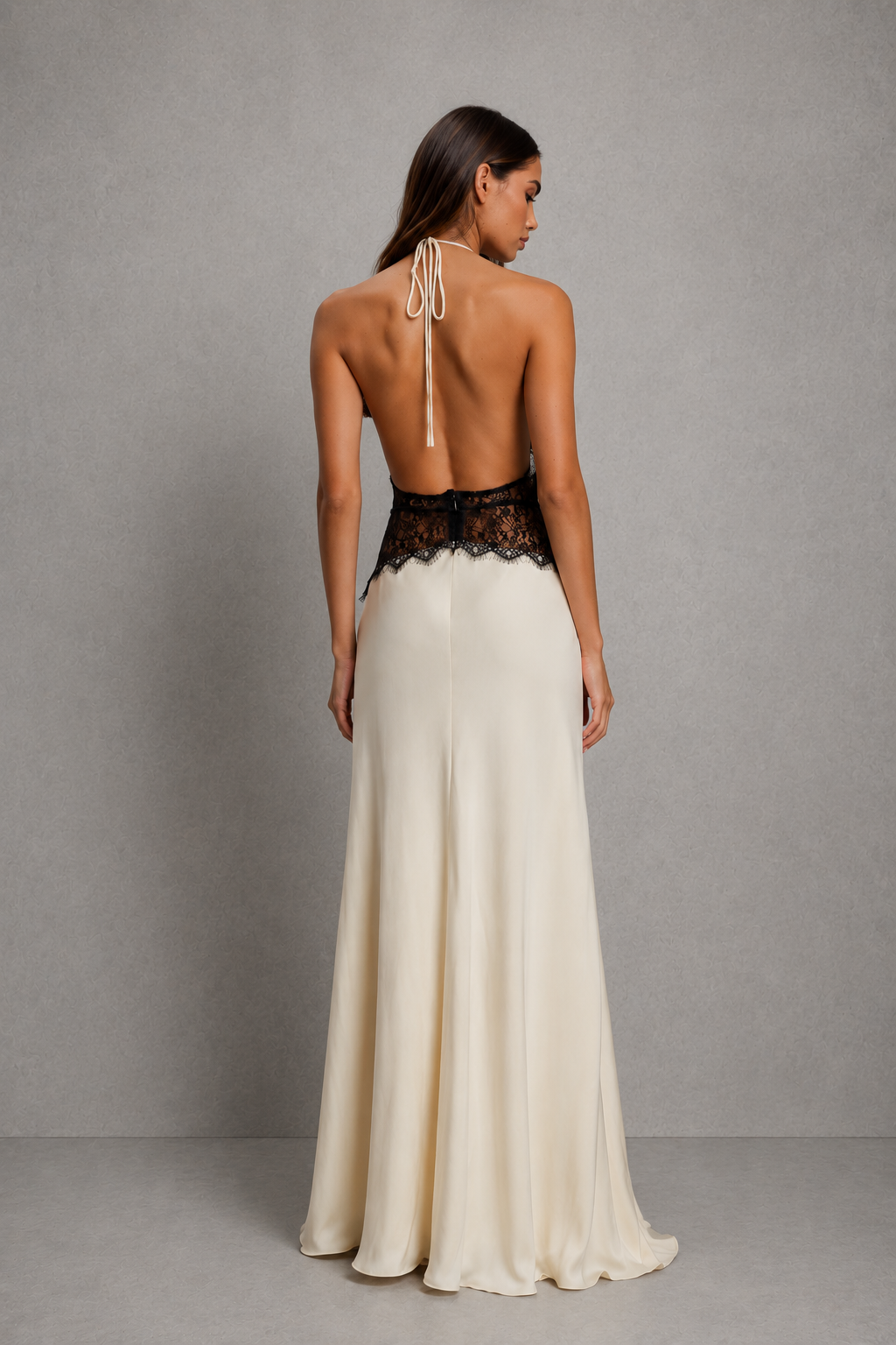 A woman shown from the back wearing a floor-length formal gown with a black lace waistband and a cream satin skirt, photographed against a plain gray studio backdrop.