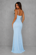 A woman modeling a light blue sleeveless maxi dress from the back, set against a textured gray studio backdrop.