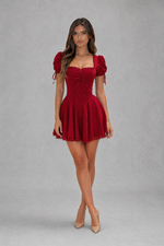 Woman wearing a red dress with puff sleeves against a gray background