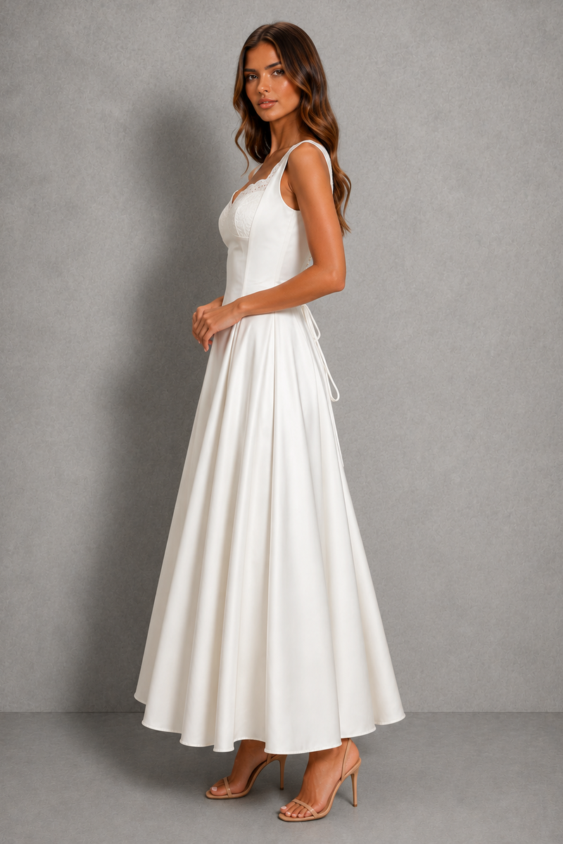 A woman modeling a sleeveless white maxi dress with a V-neckline and a flowing skirt, standing against a textured gray studio backdrop.