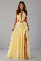 Woman wearing a yellow evening gown with a high slit on a gray background