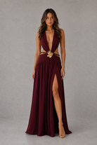 Woman wearing a burgundy evening gown with a high slit on a gray background