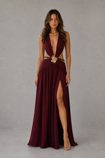 Woman wearing a burgundy evening gown with a high slit on a gray background