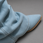 Women’s light blue denim knee-high boots with ruched shafts, pointed toes and square block heels.