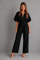 Woman wearing a black jumpsuit against a gray background