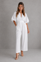 Woman wearing a white jumpsuit against a gray background