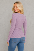 Woman wearing a purple ribbed sweater and blue jeans against a white background