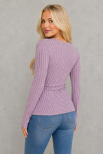 Woman wearing a purple ribbed sweater and blue jeans against a white background