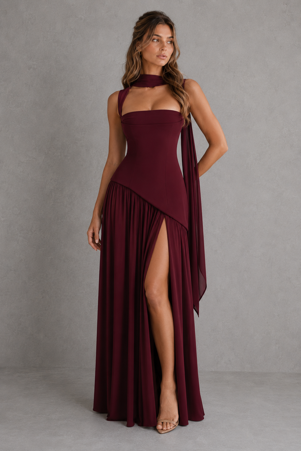 Woman wearing a burgundy evening gown with a slit on a gray background