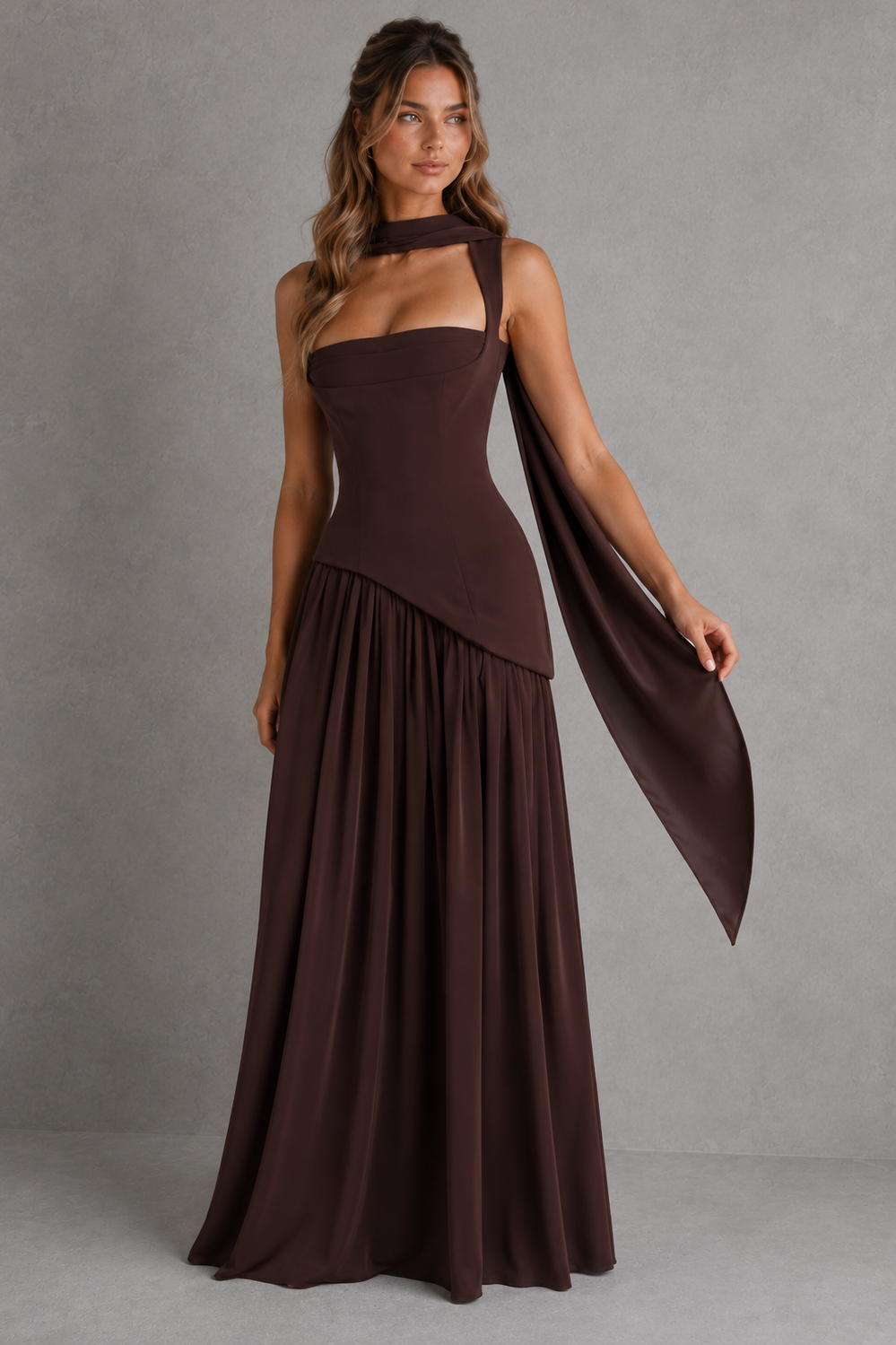 Woman wearing a brown halter neck dress with a draped fabric against a gray background