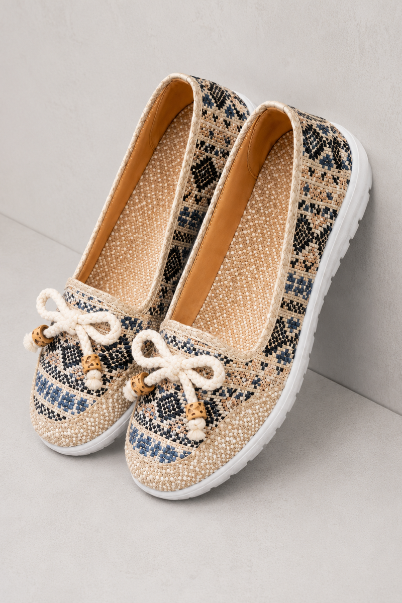 A pair of women's slip-on shoes with a beige woven snakeskin pattern, featuring white rope bows with small gold and white beads on the toes, and white soles.