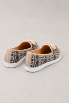 A pair of slip-on woven sneakers with a beige, black, and blue snakeskin pattern, featuring thick white soles and rope laces, shown on a neutral gray background.