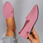 Pink knitted loafers being held up against a gray background
