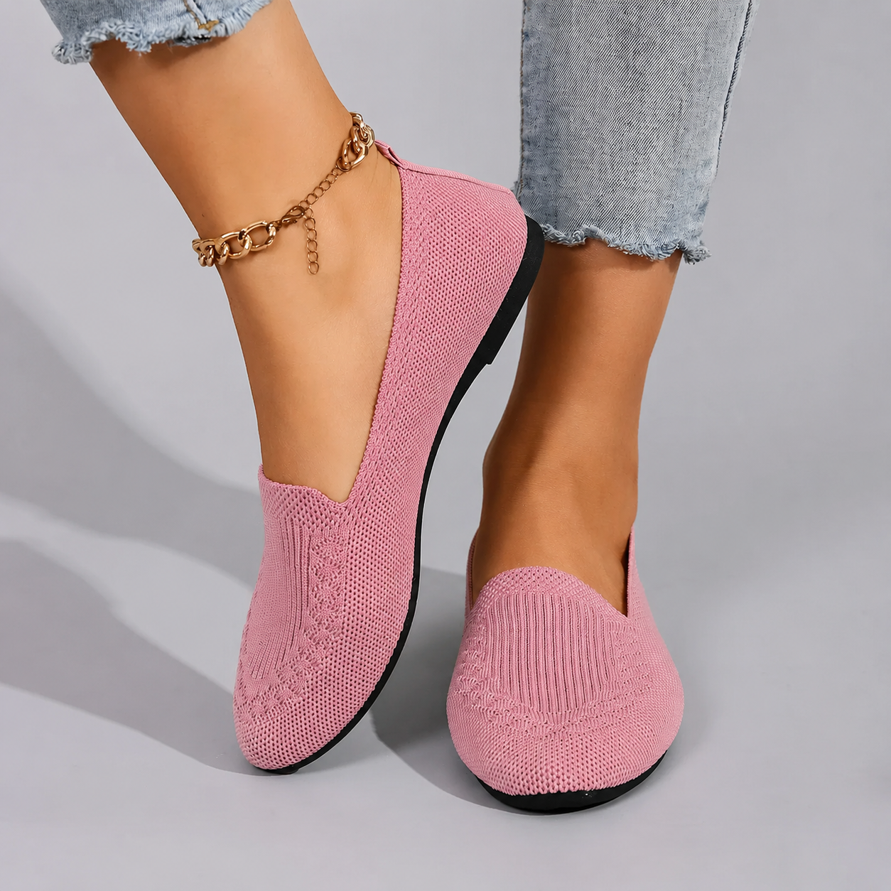 Pink slip-on shoes worn with light blue jeans on a gray background