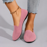 Pink slip-on shoes worn with light blue jeans on a gray background