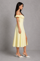 Woman wearing a yellow off-shoulder dress with a slit on a gray background