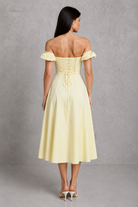 Woman wearing a light yellow off-shoulder dress against a gray background