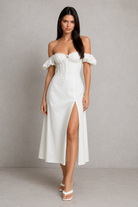 Woman wearing a white off-shoulder dress with a slit on a plain background