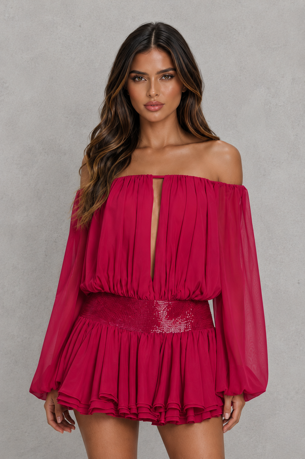 A woman modeling a bright fuchsia off-the-shoulder mini dress with long sheer sleeves, a keyhole neckline, and a ruffled peplum skirt against a textured gray studio background.