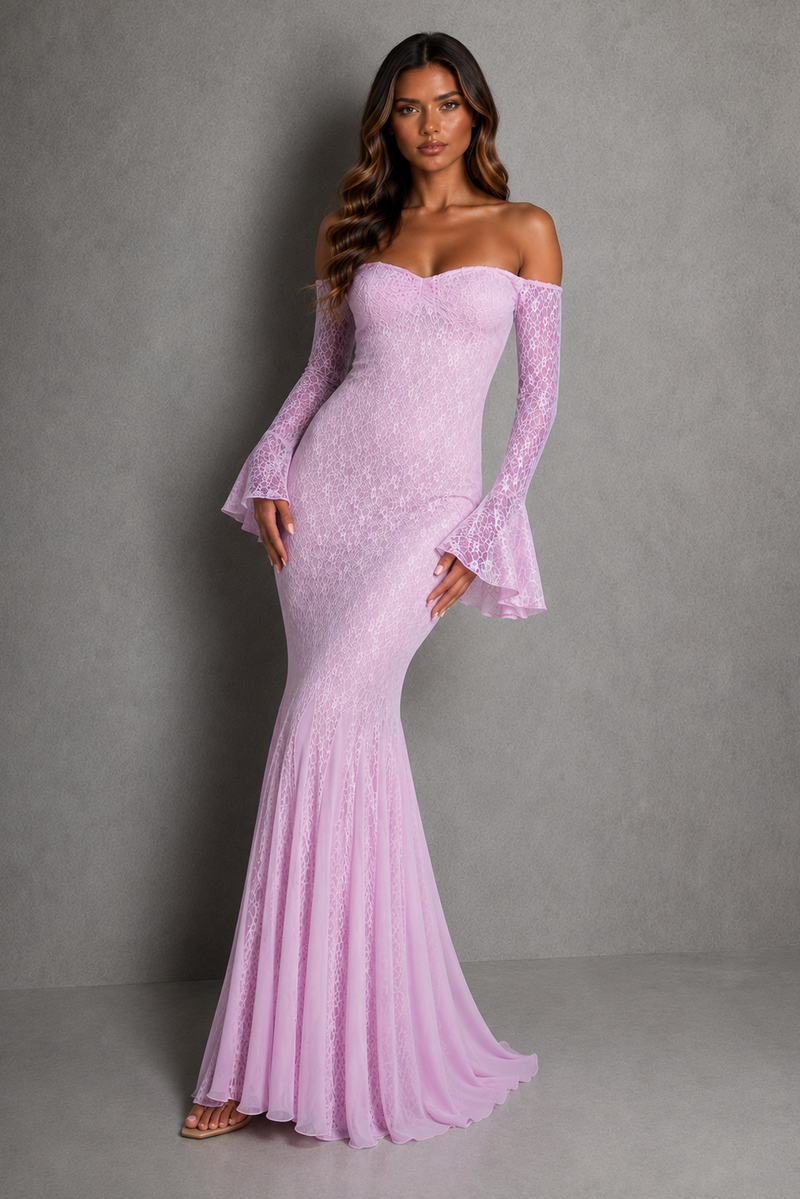 A woman modeling a light pink off-the-shoulder lace mermaid gown with long flared sleeves, standing against a textured gray studio backdrop.