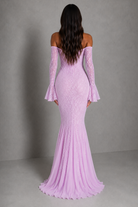 A woman viewed from the back wearing a lavender off-the-shoulder mermaid gown with long flared sleeves and a fitted lace-embroidered bodice, photographed against a plain gray studio backdrop.