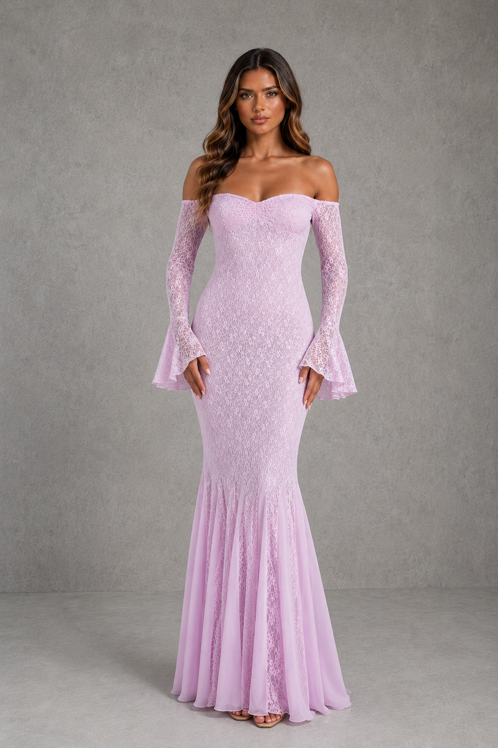 A woman modeling a lavender off-the-shoulder lace gown with long flared sleeves and a fitted mermaid-style skirt against a textured gray studio backdrop.