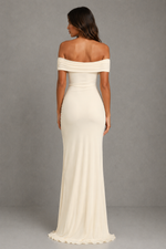 An off-the-shoulder floor-length gown in a warm ivory or cream color, shown from the back on a model against a neutral gray studio background.