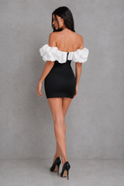 Woman wearing a black dress with white ruffled sleeves against a gray background