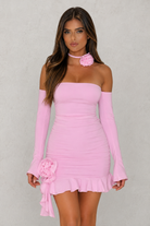 Woman wearing a pink off-shoulder dress with floral details on a gray background
