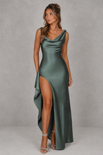 Woman wearing a green satin dress with a high slit on a gray background