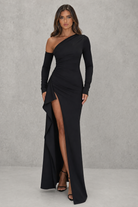Woman wearing a black one-shoulder dress with a slit on a gray background
