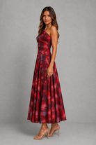 A woman modeling a strapless red and black floral maxi dress with a fitted bodice and flowing skirt, paired with nude high-heeled sandals against a gray studio background.