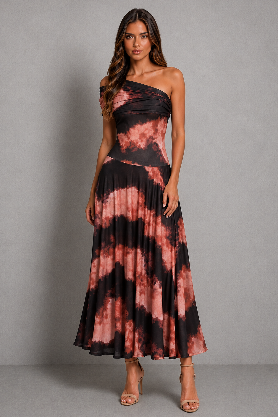 A woman modeling a one-shoulder maxi dress with a black and dusty rose tie-dye pattern, standing against a neutral gray studio background.