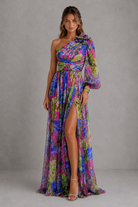 Woman wearing a colorful one-shoulder dress with a slit on a gray background
