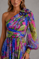 Woman wearing a colorful one-shoulder dress with floral patterns against a neutral background