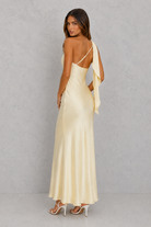 Woman wearing a long, light-colored dress with thin straps against a plain background