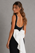 Woman wearing a black dress with a white bow on a gray background