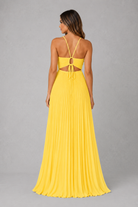 A woman modeling a bright yellow sleeveless maxi dress from the back, featuring a pleated skirt and a cutout back with tie straps, set against a neutral gray studio background.