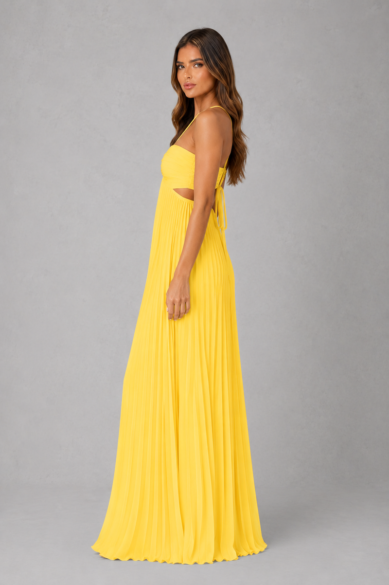A woman modeling a bright yellow sleeveless maxi dress with a halter-style neckline, side cutouts, and a flowing pleated skirt, photographed against a plain gray studio background.