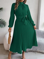 Woman wearing a green dress in a room with a white wall and striped rug.