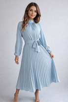 Woman wearing a light blue dress with a belt on a plain background