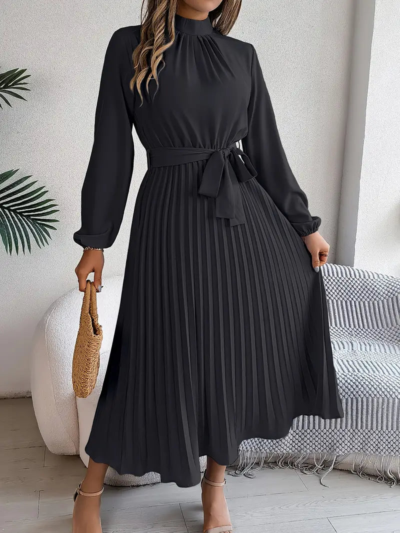 Woman wearing a black dress with long sleeves in a room with a white wall and a plant.