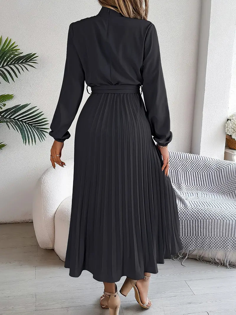 Woman wearing a black pleated dress in a room with a couch and plant.