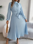 Woman wearing a light blue dress with pleated skirt in a room setting.