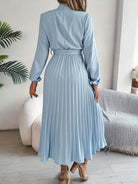 Woman wearing a light blue pleated dress in a room with a couch and plant.