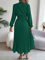 Green dress worn by a person in a room with a white wall and a plant.