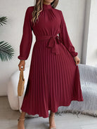 Woman wearing a burgundy pleated dress in a room with a couch and plant.