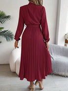 Person wearing a burgundy pleated dress in a room with a white wall and plant.